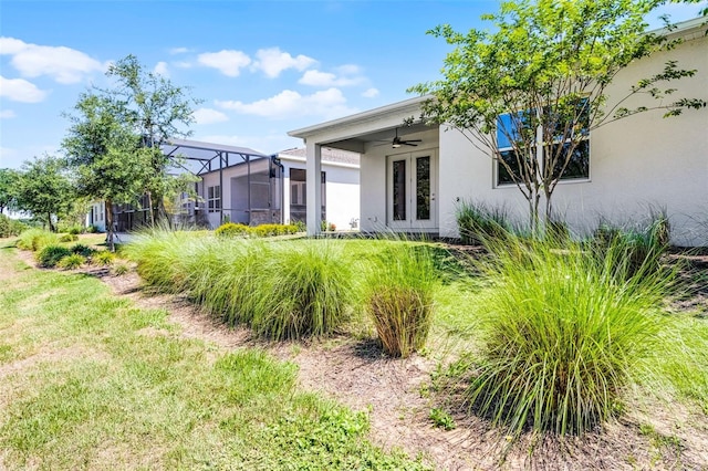 rear view of house with glass enclosure, french doors, ceiling fan, a yard, and stucco siding