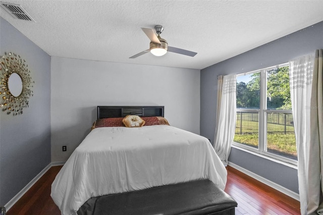 bedroom with a textured ceiling, baseboards, visible vents, wood finished floors, and ceiling fan