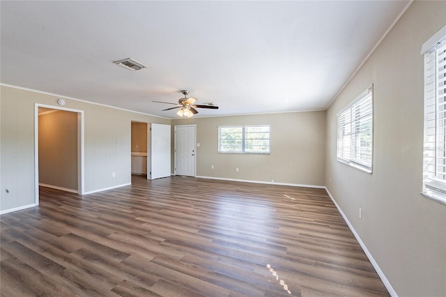 empty room featuring dark wood finished floors, visible vents, ornamental molding, baseboards, and ceiling fan