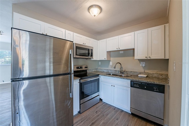 kitchen with white cabinets, light wood finished floors, light stone counters, a sink, and appliances with stainless steel finishes