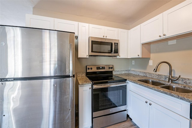 kitchen with white cabinets, light stone countertops, stainless steel appliances, and a sink