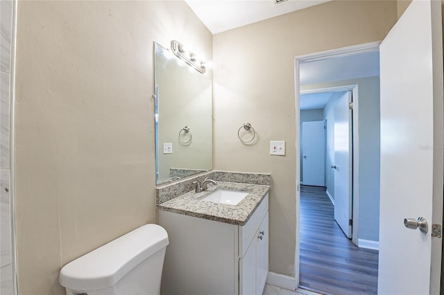 half bath featuring toilet, vanity, wood finished floors, and baseboards