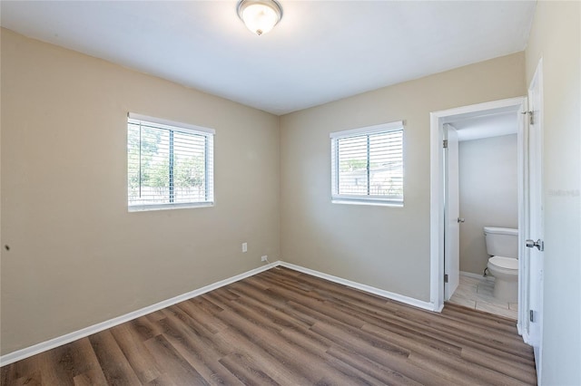unfurnished bedroom with wood finished floors, baseboards, and connected bathroom