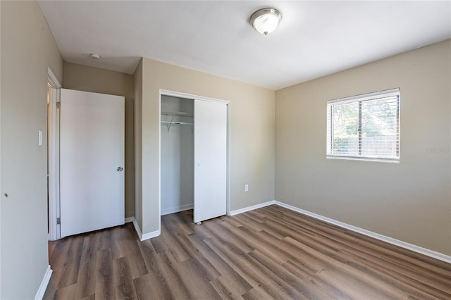 unfurnished bedroom featuring baseboards, wood finished floors, and a closet