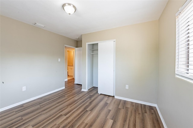 unfurnished bedroom featuring baseboards, wood finished floors, visible vents, and a closet