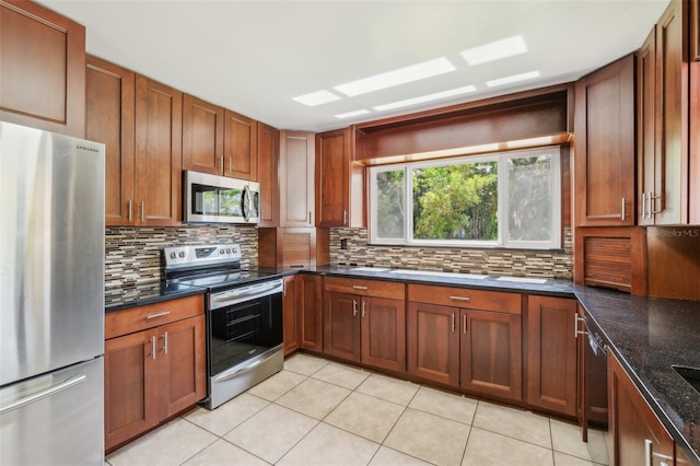 11352 Persimmon Blvd, West Palm Beach, FL 33411 - kitchen featuring appliances with stainless steel finishes, tasteful backsplash, light tile patterned flooring, dark stone countertops, and brown cabinets