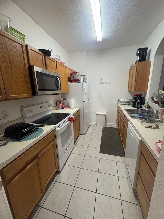 kitchen with white appliances, brown cabinetry, a textured ceiling, light countertops, and a sink