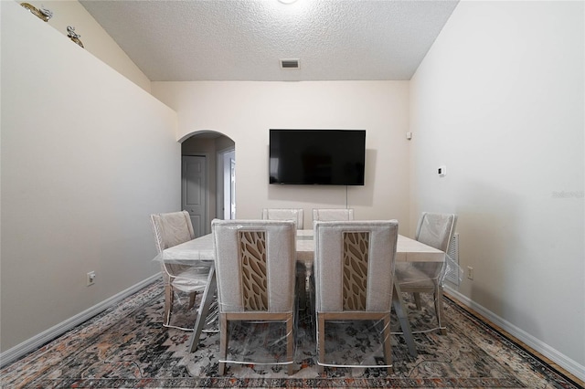 dining area featuring visible vents, baseboards, arched walkways, and a textured ceiling