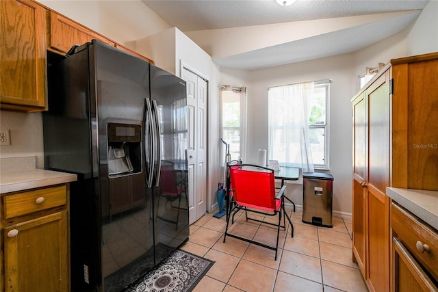 kitchen featuring light countertops, brown cabinetry, black fridge, and lofted ceiling