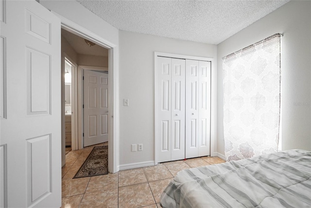 bedroom with a textured ceiling, a closet, light tile patterned floors, and baseboards