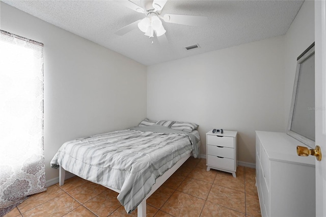 bedroom with visible vents, ceiling fan, light tile patterned floors, and a textured ceiling