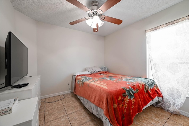 bedroom featuring a textured ceiling, light tile patterned floors, baseboards, and a ceiling fan