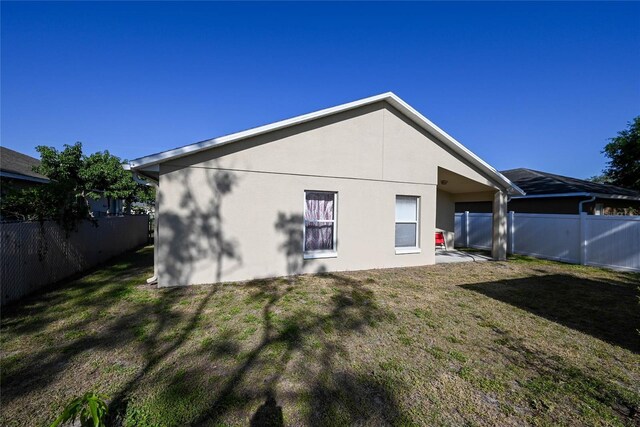 rear view of house with a lawn, a fenced backyard, and stucco siding