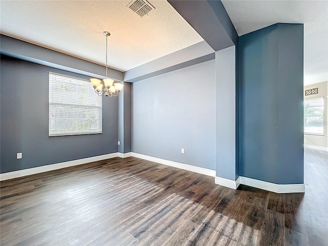 empty room featuring an inviting chandelier, wood finished floors, visible vents, and baseboards