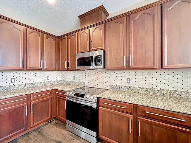 kitchen featuring a textured ceiling, decorative backsplash, light wood-style floors, appliances with stainless steel finishes, and light stone countertops