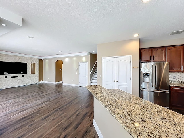 kitchen with arched walkways, stainless steel refrigerator with ice dispenser, light stone countertops, and recessed lighting