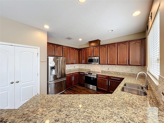 kitchen with backsplash, appliances with stainless steel finishes, light stone counters, and a sink