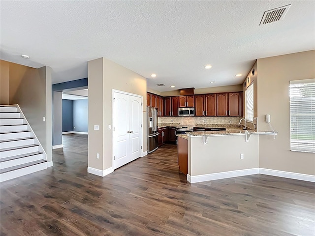 kitchen with a kitchen breakfast bar, visible vents, dark wood-type flooring, a peninsula, and appliances with stainless steel finishes