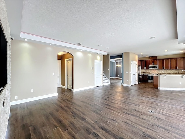 unfurnished living room with arched walkways, a textured ceiling, dark wood finished floors, recessed lighting, and stairway