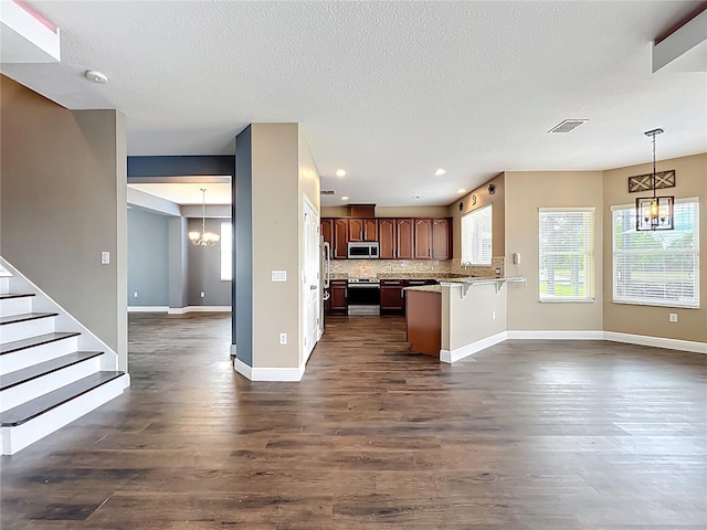 kitchen with stainless steel appliances, a peninsula, dark wood finished floors, open floor plan, and baseboards