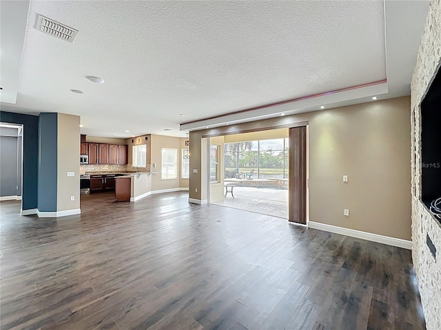 unfurnished living room featuring dark wood-type flooring, a textured ceiling, visible vents, and baseboards