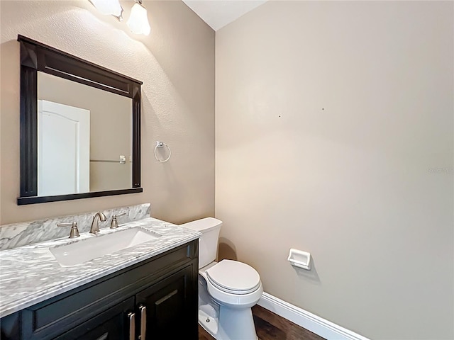 half bathroom with baseboards, wood finished floors, vanity, and toilet