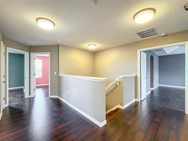 hall with an upstairs landing, a textured ceiling, visible vents, and hardwood / wood-style floors
