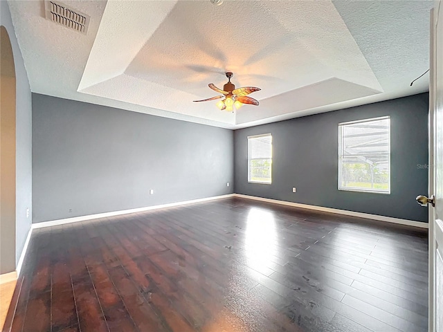 spare room with wood finished floors, a tray ceiling, visible vents, and a textured ceiling