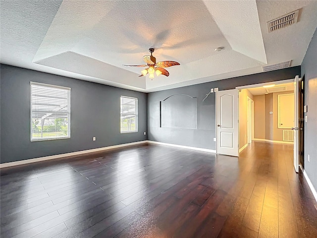 empty room with a raised ceiling, a textured ceiling, and hardwood / wood-style flooring