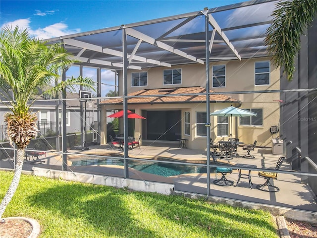 rear view of property with an outdoor pool, glass enclosure, a yard, stucco siding, and a patio
