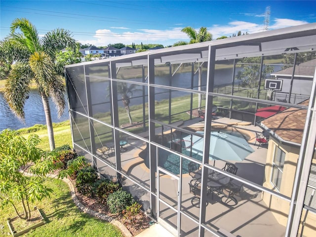 pool featuring glass enclosure, a water view, and a patio