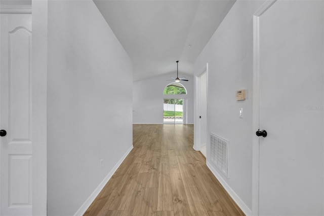 hall featuring light wood-style floors, visible vents, baseboards, and vaulted ceiling