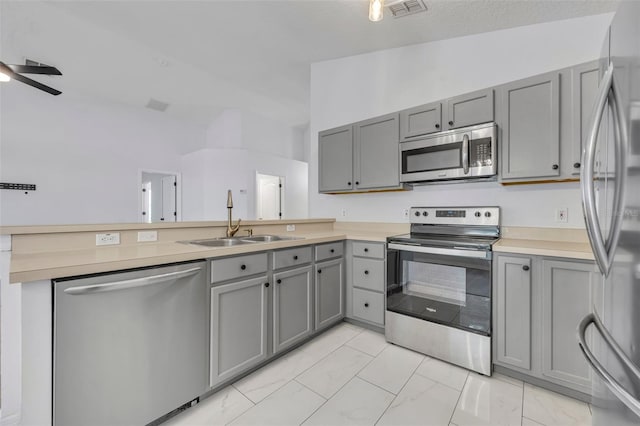 kitchen featuring a peninsula, a sink, gray cabinetry, and stainless steel appliances