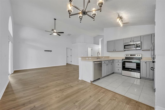 kitchen featuring open floor plan, a peninsula, ceiling fan with notable chandelier, gray cabinets, and stainless steel appliances