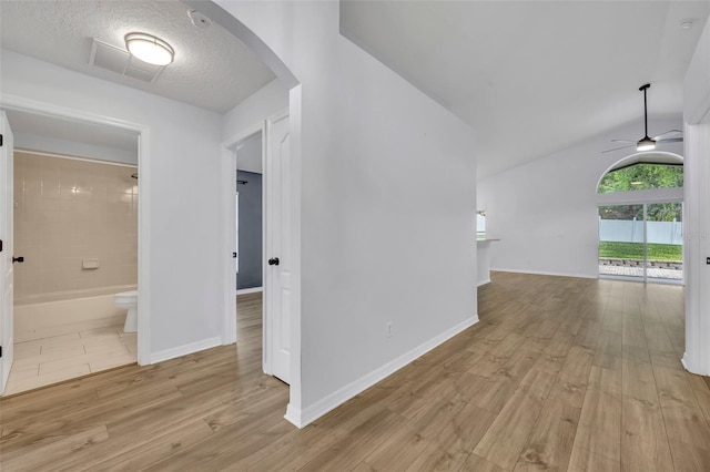 hallway featuring visible vents, light wood-style flooring, arched walkways, and baseboards