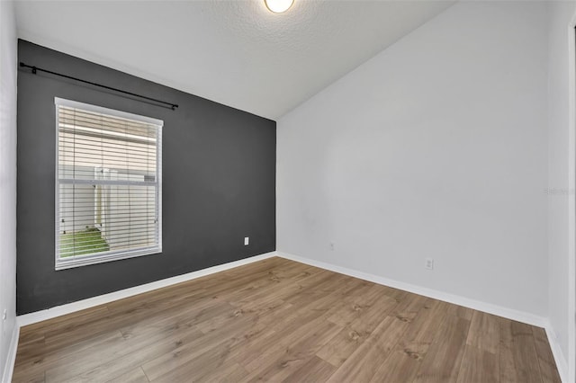 empty room featuring a textured ceiling, baseboards, vaulted ceiling, and wood finished floors