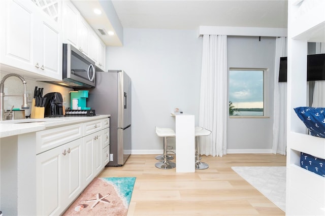 8800 Bay Pines Blvd Unit 306, Saint Petersburg, FL 33709 - kitchen with light wood-style flooring, backsplash, white cabinetry, light countertops, and appliances with stainless steel finishes