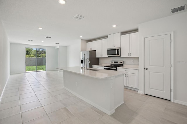 1839 Brekey Way, Zephyrhills, FL 33541 - kitchen featuring appliances with stainless steel finishes, a sink, white cabinetry, light tile patterned floors, and an island with sink