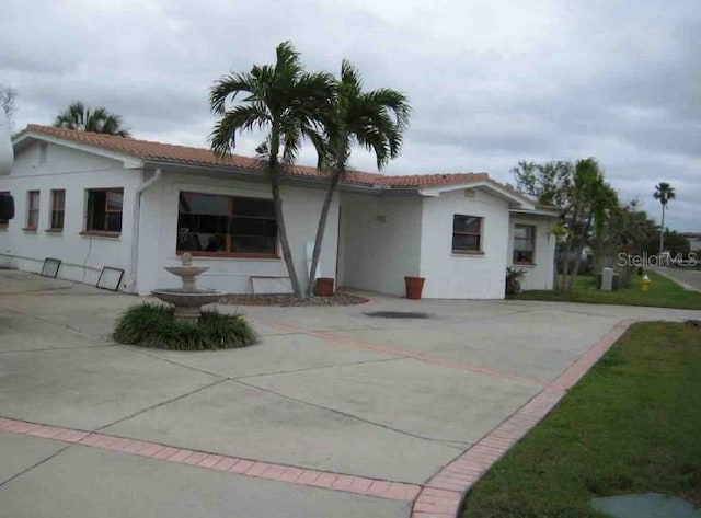 rear view of property with driveway, stucco siding, and a tile roof