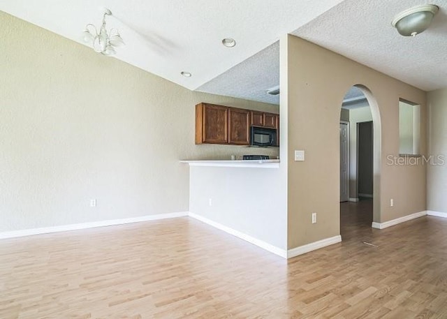 2503 SE 18th Cir, Ocala, FL 34471 - kitchen featuring light wood-style floors, black microwave, arched walkways, a textured ceiling, and baseboards