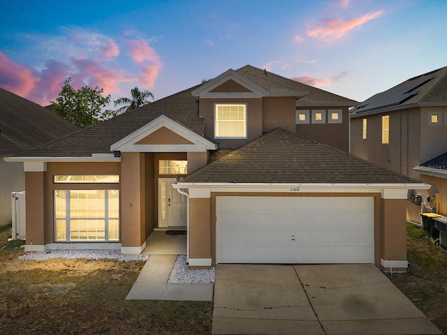 traditional home featuring an attached garage, roof with shingles, stucco siding, and concrete driveway