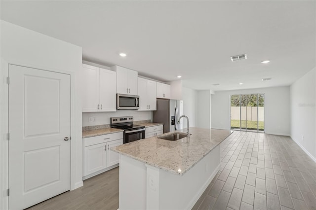 1861 Brekey Way, Zephyrhills, FL 33541 - kitchen featuring stainless steel appliances, a sink, white cabinetry, an island with sink, and light wood-style floors