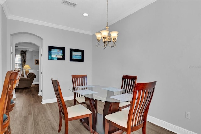 dining area featuring visible vents, crown molding, an inviting chandelier, wood finished floors, and arched walkways