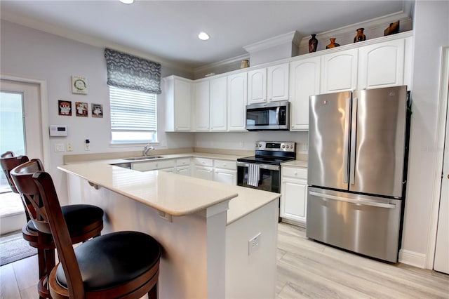 kitchen with crown molding, a sink, a breakfast bar area, stainless steel appliances, and white cabinetry
