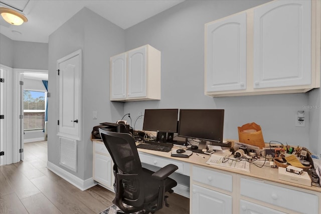 office area with light wood-type flooring, baseboards, built in desk, and visible vents