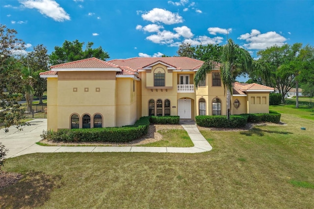 mediterranean / spanish-style home featuring a balcony, stucco siding, a tiled roof, and a front lawn