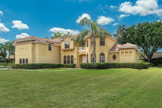 mediterranean / spanish-style house featuring a balcony, stucco siding, a tiled roof, and a front yard