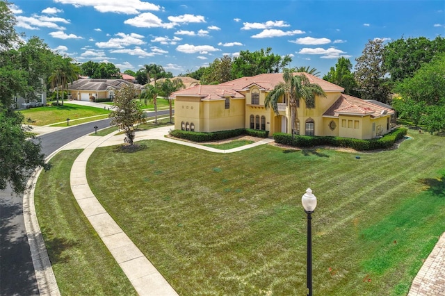 mediterranean / spanish house featuring a front lawn, a tiled roof, and stucco siding