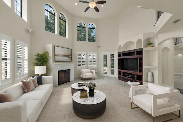 living room with a ceiling fan, recessed lighting, a glass covered fireplace, visible vents, and a towering ceiling