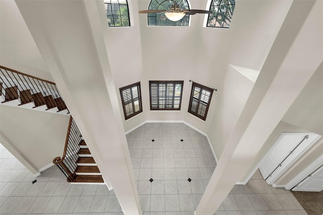 stairs featuring a ceiling fan, baseboards, tile patterned floors, and a towering ceiling